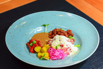 Vegetable salad with sause served on a blue plate on dark rustic wooden table in restaurant.