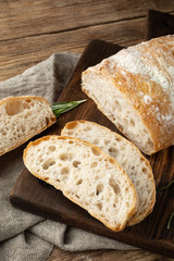 Delicious homemade sliced Italian ciabatta bread on a wooden cutting board. Close-up. - obrazy, fototapety, plakaty