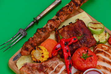 Top view of grilled meal of steak and vegetables spread out on rustic wooden board over bright green background