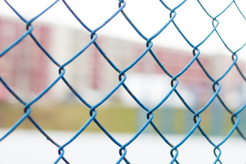 Fence on the sky, blue mesh fence, chain link fence, building back background. Soft focus.