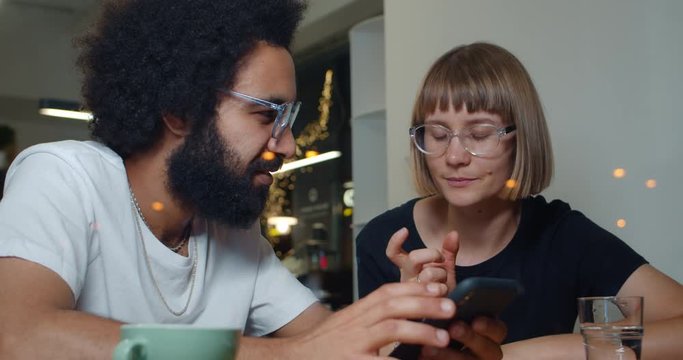 Man and woman sitting at cafe and discussing work moments in unformal setting. Two people talking to each other while looking at smartphone screen. Concept of communication and tech.