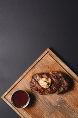 Top view of grilled bbq smoked meat steak with sauce on dark wooden board on black background, flat lay, copy space