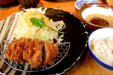 Set pork tonkatsu rice, fried pork on a black plate, paired with cabbage The side has a bowl of rice and a sauce cup. All put on the table.