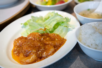 Stir fried shrimp with spicy sauce or Ebi Chlli on a white plate with lettuce With steamed rice in a bowl and soup beside the plate Is a popular Chinese food in Japan.
