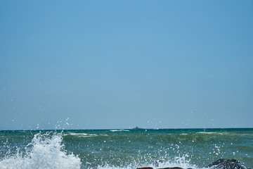 Image of the sea shore. In the background is a warship.