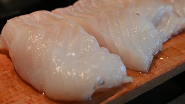 Close up shot of a cod fillet placed on a wooden cutting board and cut into portions.
