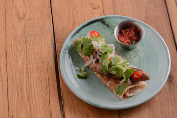 Meat sausages with fresh greenery on lavash bread with sauce in a sauce pan served on a blue plate over wooden table.