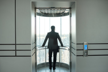 Fototapeta na wymiar Young elegant businessman in formalwear standing in elevator with open door