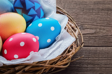 Closeup part of a nest with colored Easter eggs on white napkins on an old rustic wooden table with copy space