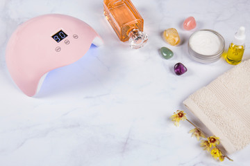 Closeup of led uv lamp for curing top cover of nail polish gel. White Marble background and stylish trendy accessories, hand cream, hand oil and parfum