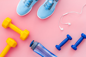 Fitness equipment. Sneakers, dumbbells, headphones on pink background top view