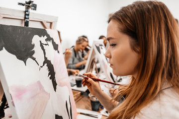 A young woman painstakingly draws her picture with brushes on easels in an art class. learning to...