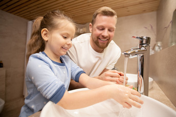 Fototapeta premium Happy young man looking at his cute little smiling daughter washing hands
