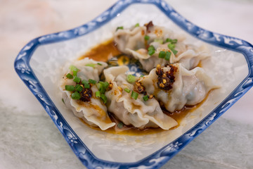 Pork dumplings are steamed topped with chilli sauce in a blue-white Chinese style dish, a Chinese dish called dim sum.