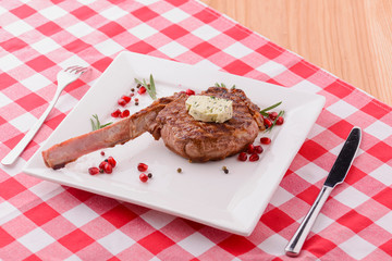 Rack of lamb served with pomegranate seeds and sauce on white plate over red plaid tablecloth....