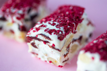 Torrone or nougat bar with nuts and red dried berries. Traditional italian dessert close up on pink background. Sweet tasty and healthy food