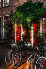 Fototapeta na wymiar Some bicycles parking near brick house wall with sunlight and beautiful red doors and green tree with red flowers in Amsterdam, Netherlands.. Bikes are staying.