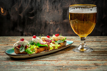 Hearty snack with different kinds of spreads on farmhouse bread served with a fresh yeast wheat beer on an old wooden table. Bruschetta with salmon, cheese, basil. Beer with foam
