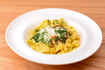 Spaghetti pasta with dill and tomato sauce served in white plate over light rustic wooden table.