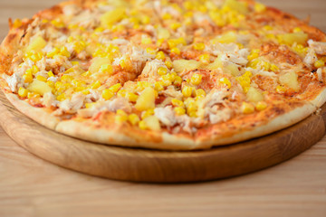 Fresh pizza with chicken meat, cheese and corn on wooden board over rustic wooden table background closeup.