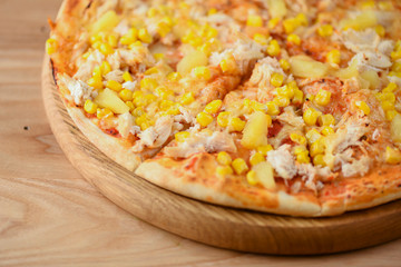 Fresh pizza with chicken meat, cheese and corn on wooden board over rustic wooden table background closeup.