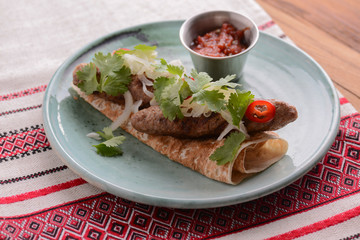 Meat sausages with fresh greenery on lavash bread with sauce in a sauce pan served on a blue plate over wooden table.