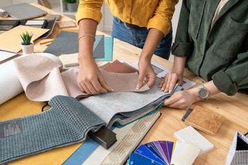 Hands of two designers of interior standing by desk and choosing fabric samples