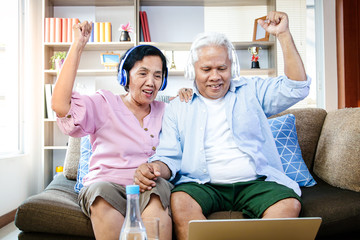 The elderly Asian couples are enjoying watching movies on TV online, on the internet. In the living room in the house. The concept of a happy life in retirement