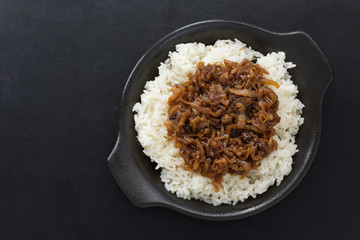 Top view of caramelized onion with rice as garnish on black plate on the black background