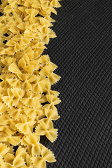 Food background - dry farfalle pasta on black background, whole wheat uncooked ingredient, space for text