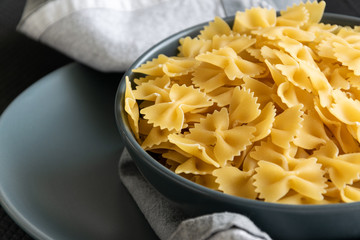 Food background - dry farfalle pasta on grey plate, whole wheat uncooked ingredient, space for text