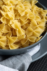 Food background - dry farfalle pasta on grey plate, whole wheat uncooked ingredient, space for text
