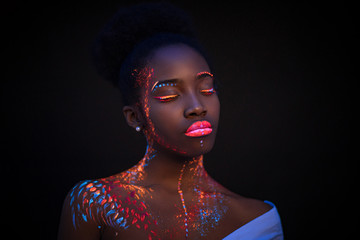 Portrait of african young woman with fluorescent makeup on face and skin that glowing in...