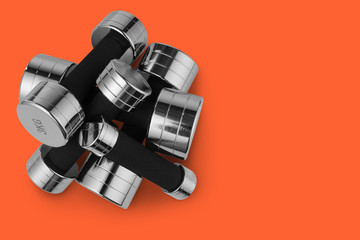 many steel chrome dumbbells lie in heap, on top of each other, sports concept, on orange background, top view