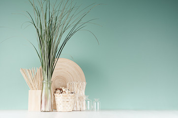 Natural soft light accessories for home decor - dried plant, wicker basket, sticks, bamboo plate, bouquet of reed, glass bottle in green mint menthe interior on white wood table.