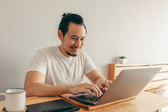 Happy Asian man is working with laptop in his apartment bedroom in concept of Work From Home and Work at Home.