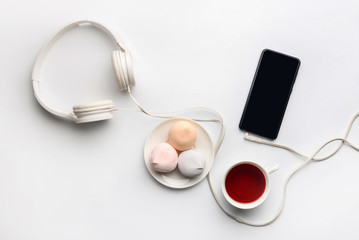 Composition, with a cup of tea, cake, headphones and a smartphone on a white background.