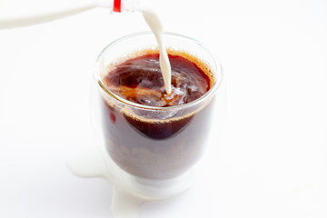 Pouring milk from milk bottle into glass cup with brewed coffee on white background
