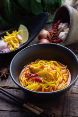 Thai noodles chicken curry in black bowl.