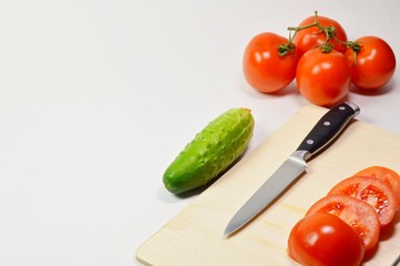 A sliced tomato and a knife on the kitchen wooden Board. Cucumber and tomato in the background. Food preparation concept.