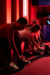 Row of young casual friends sitting on bench and putting on bowling shoes