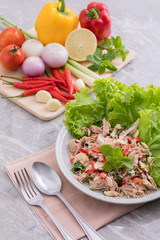 On a white plate there is a tuna salad with a variety of herbs and green oak vegetables are placed and next to herbs are placed on a wooden cutting board.