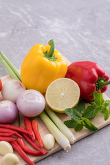 Herbs used for making soup and salad are tomatoes, lemongrass, onions, garlic, chili, lemon and mint leaves. All placed on a wooden cutting board.