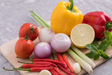 Herbs used for making soup and salad are tomatoes, lemongrass, onions, garlic, chili, lemon and mint leaves. All placed on a wooden cutting board.