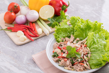 On a white plate there is a tuna salad with a variety of herbs and green oak vegetables are placed and next to herbs are placed on a wooden cutting board.
