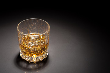 Half-full glass of whiskey is on a dark table