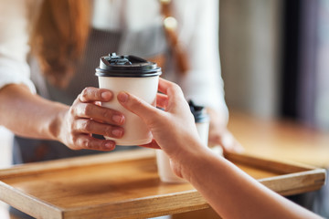 A waitress holding and serving paper cups of hot coffee to customer in cafe
