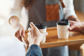 A waitress holding and serving paper cups of hot coffee to customer in cafe
