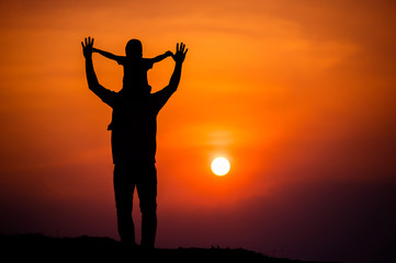 Fototapeta premium silhouette of a family with a boy riding his father's neck happily against the sunset sky