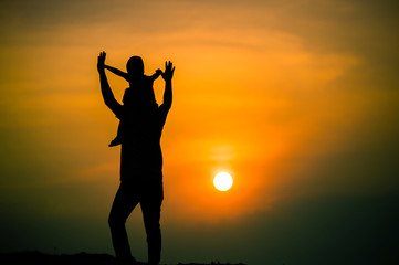 Fototapeta premium silhouette of a family with a boy riding his father's neck happily against the sunset sky